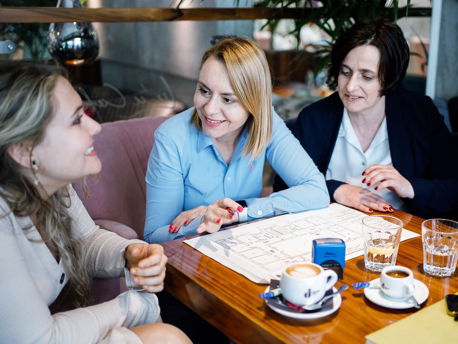 Trzy uśmiechnięte kobiety, pracowniczki Centrum Wsparcia, siedzą przy stole w kawiarni.